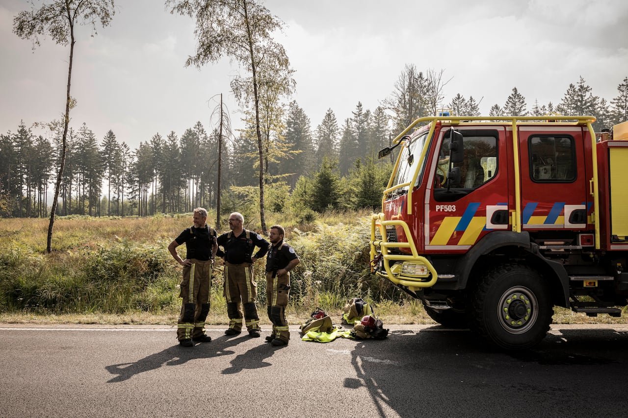 default-37 Three firefighters stand near an emergency car near a wildfire.